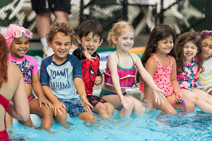 smiling children sitting on the edge of a pool with their feet in the water