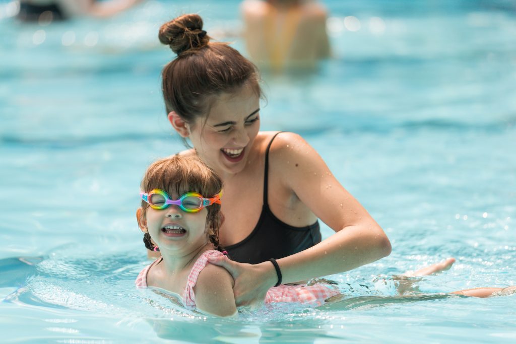 Instructor guiding a young girl swimming face down to practice proper stroke form