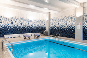 Indoor pool with white-and-blue mosaic walls, starting blocks, and a metal ladder at the edge.