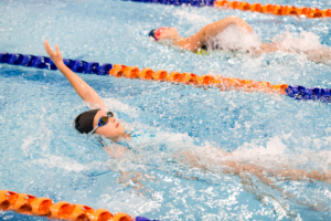 Swimmers racing in a pool with orange lane dividers and splashing water around them.
